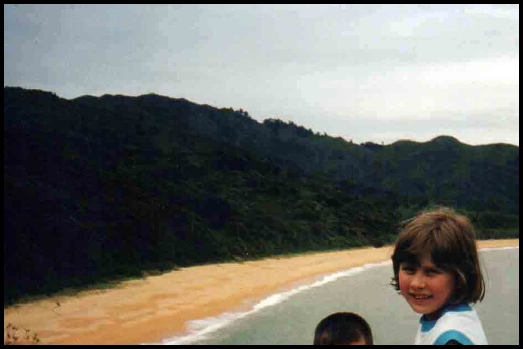 Young girl smiles at the camera with one of the Tasman region's golden sand beaches behind her.