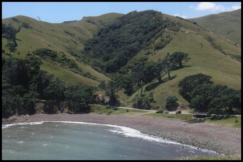 A high angle shot shows a sweeping stony beach below and steep farmland.