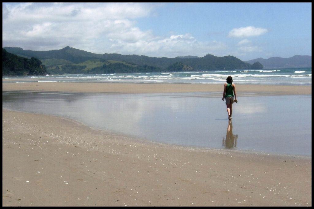 A solo woman walks away from the camera down Matarangi Beach.