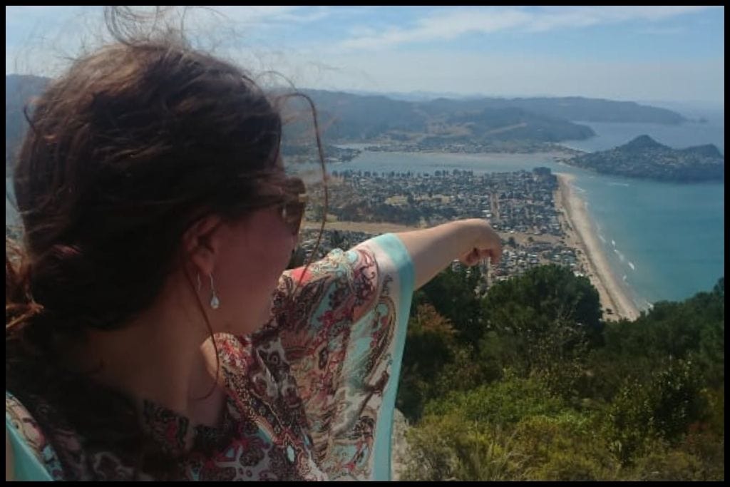Side profile of a woman at the summit of Mount Pauanui as she points down toward Pauanui Beach and Mount Paku.