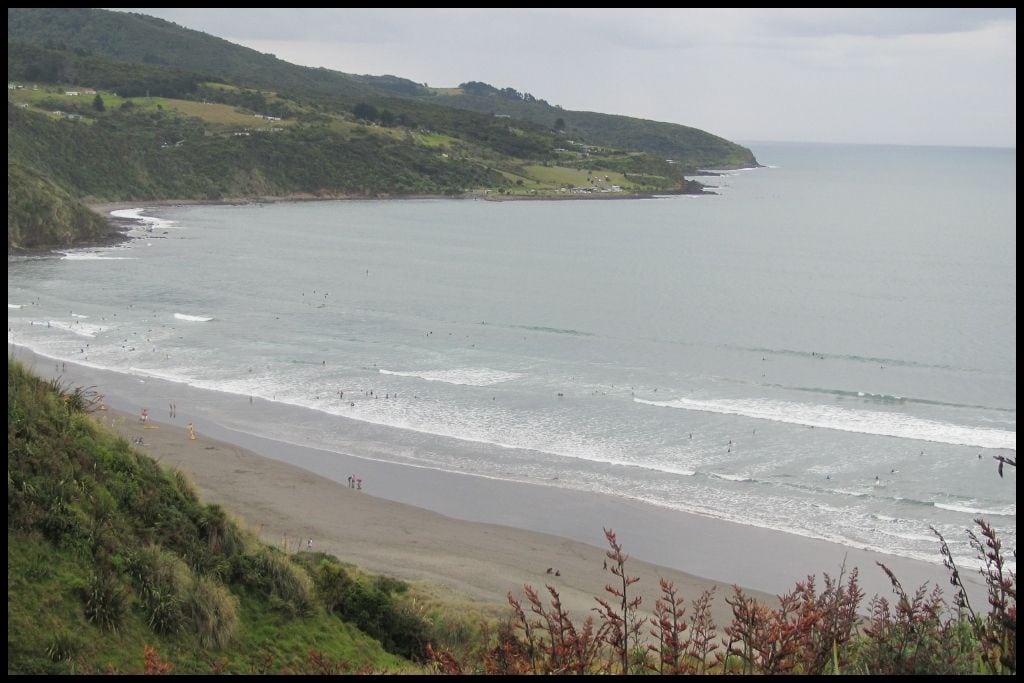 A high angle of Ngarunui Beach and all the surfers in the breaks as little dots, below.