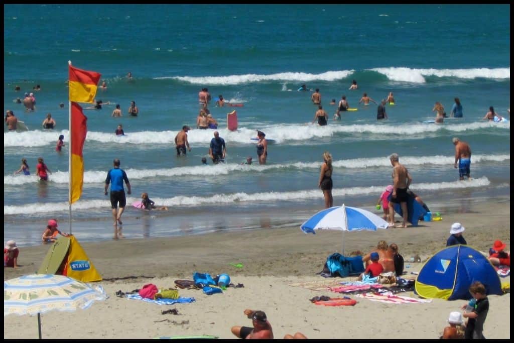 Surf breaks at Whangamata Beach - dotted with beach goers coming and going from the water.