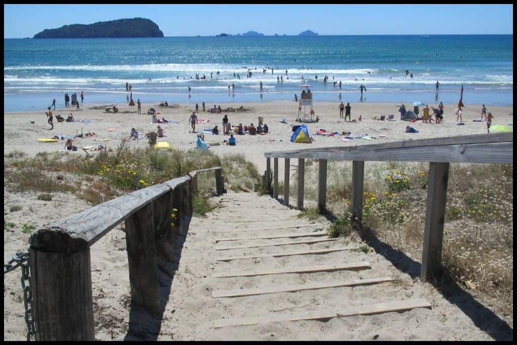 A stairway made of wood leads down to a busy beach scene at Whangamata on a summer's day.