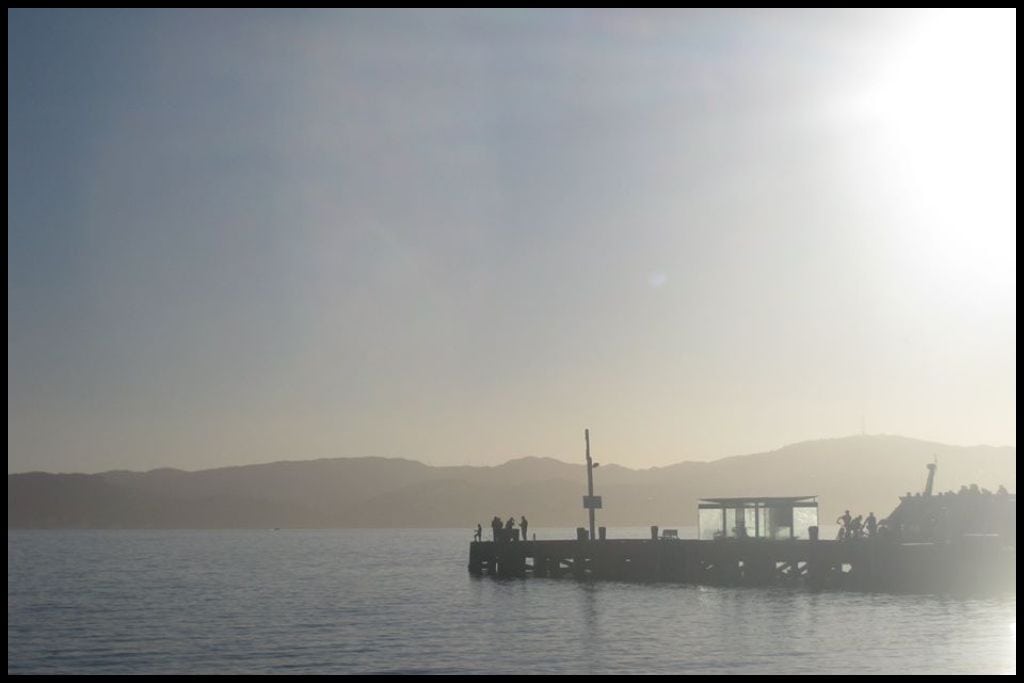 A hazy late afternoon shot of Wellington Harbour as seen from the CBD with a wharf silhouetted against the skyline.