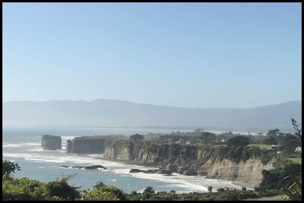 Sheer cliffs and pounding sea pictured on a fine day from a lookout higher up.