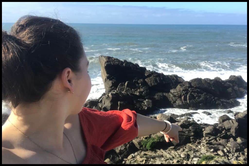 Side profile of a young woman pointing down toward the Cape Foulwind seal colony.