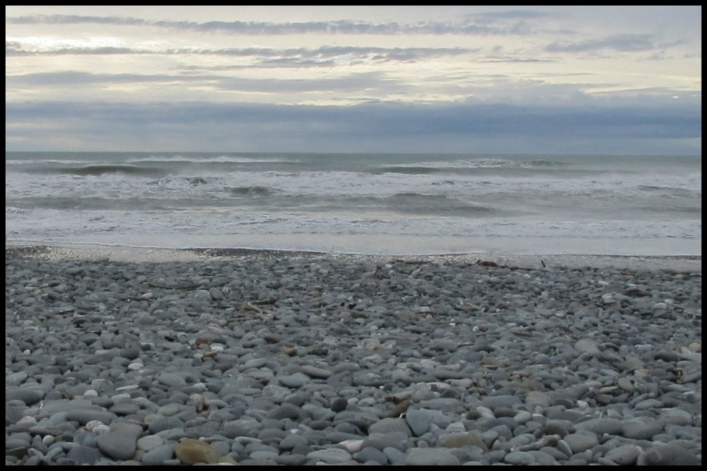A low angle shot shows the crashing surf and rocky beach of the Greymouth coastline.